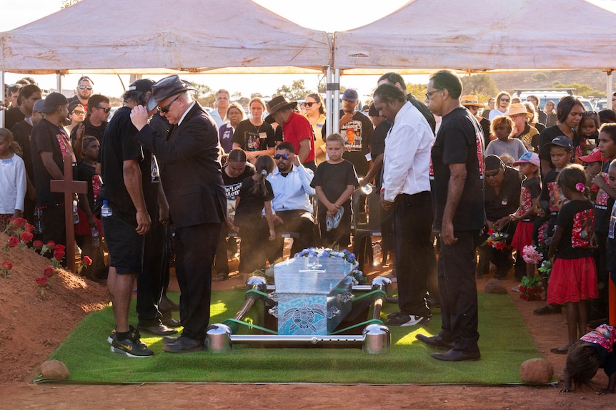 A group of people dressed in black surrounding a blue dot-painted casket being lowered into the ground. 