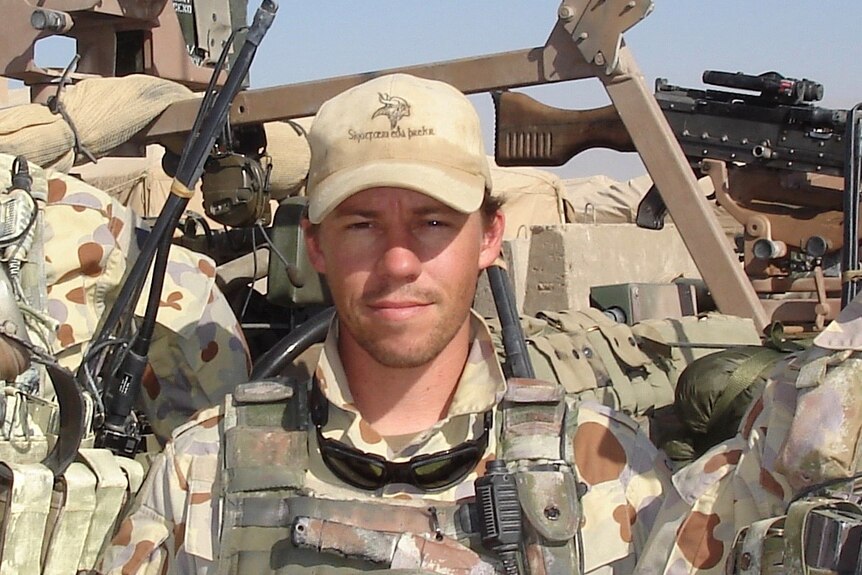 Craig McGrath standing in front of military hardware while on tour in Afghanistan