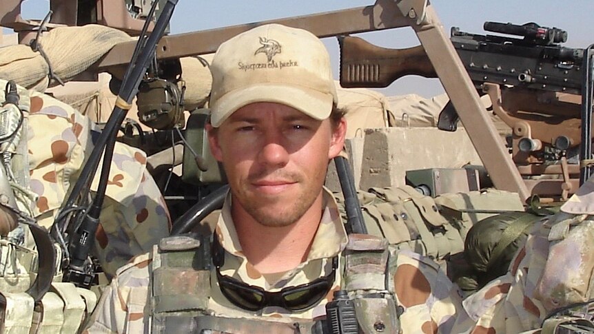 Craig McGrath standing in front of military hardware while on tour in Afghanistan