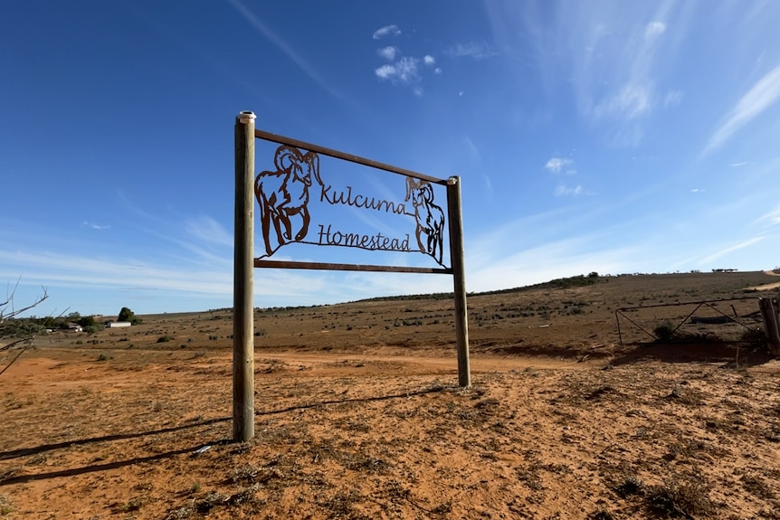 A sign reads "Kulcurna Homestead" with two rams on either side. The ground is red dirt and sky is blue.