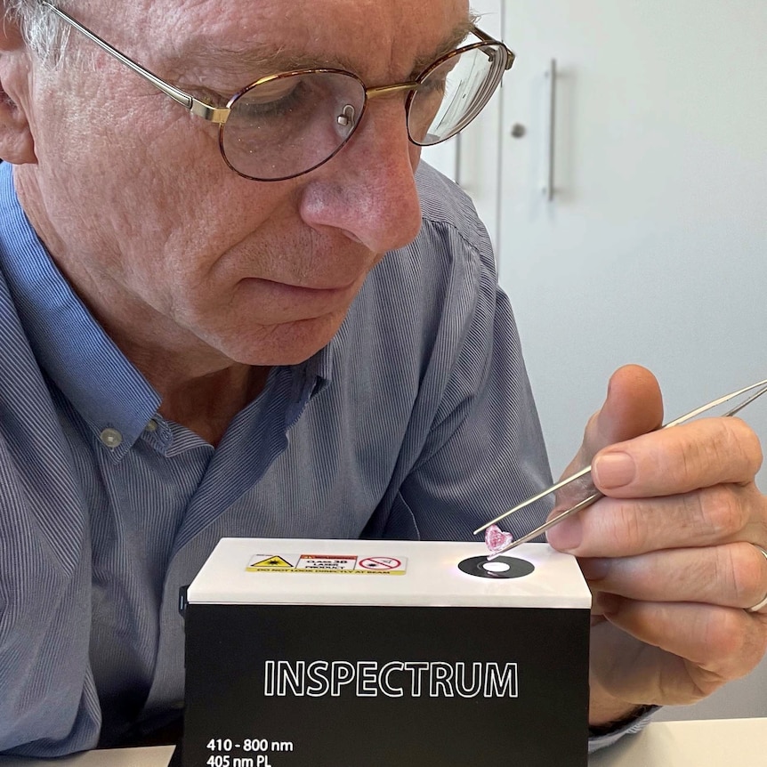 A man wearing glasses holds a pair of tweezers with a diamond.