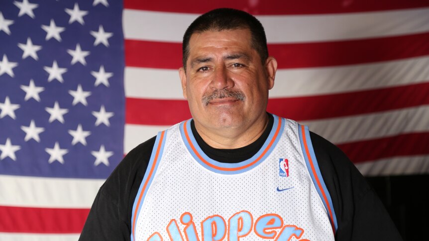 Man wearing basketball jersey stands in front of US flag.