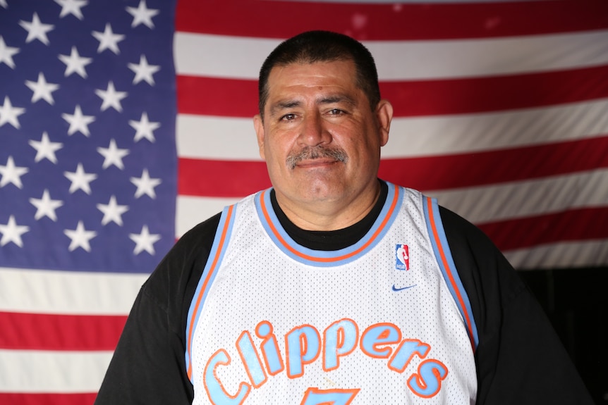 Man wearing basketball jersey stands in front of US flag.