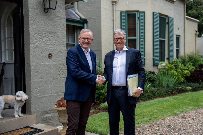 Two men wearing suits shake hands and smile.