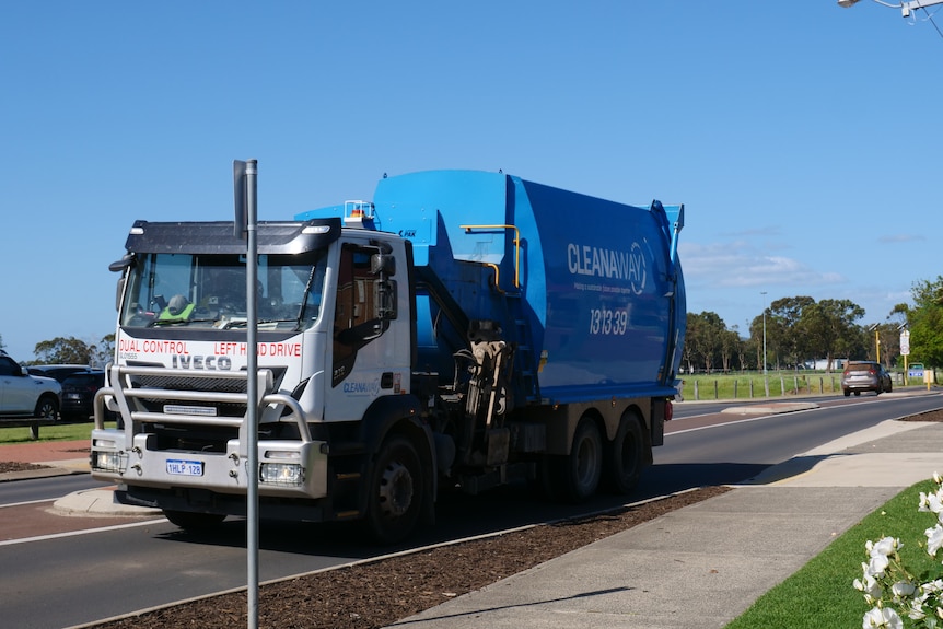 A blue rubbish truck with the words 'cleanaway' written on the side driving through a town