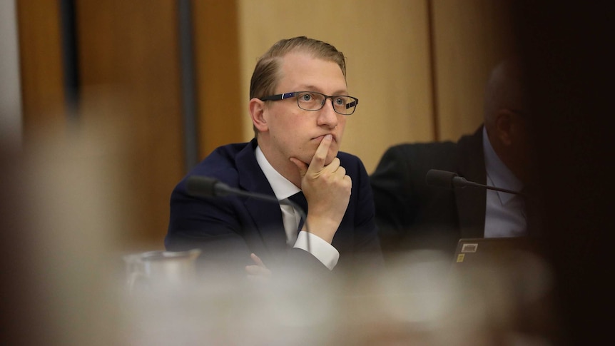 Liberal Senator James Paterson sitting in an estimates committee, wearing glasses and resting his head on his hand.