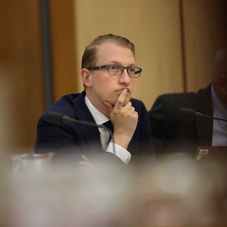 Liberal Senator James Paterson sitting in an estimates committee, wearing glasses and resting his head on his hand.