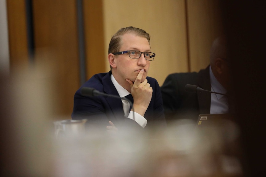 Liberal Senator James Paterson sitting in an estimates committee, wearing glasses and resting his head on his hand.