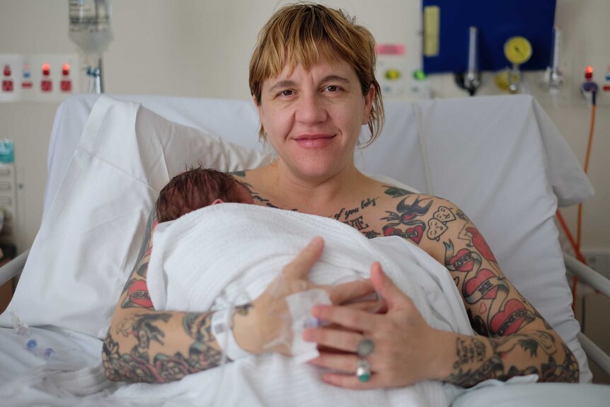 Emma Price sitting up in a hospital bed cradling her newborn bay, Bertie. July 2017