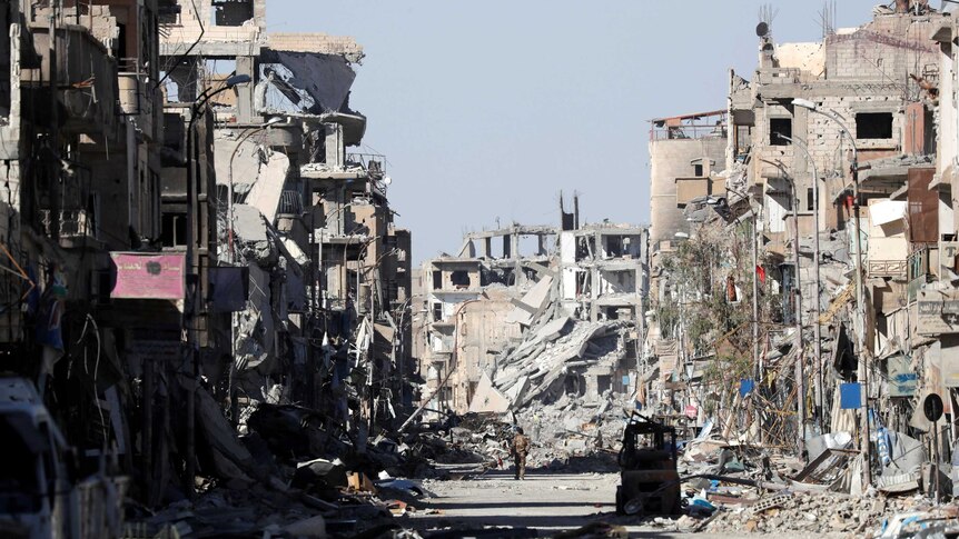 A man walks down a city street which has been destroyed by bombing