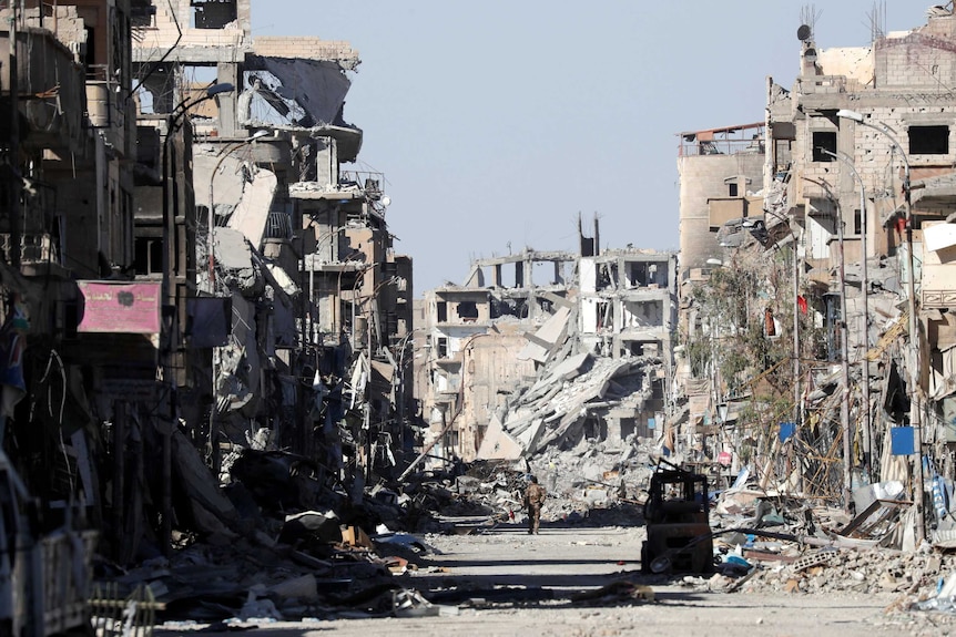 A soldier walks down a city street which has been destroyed by bombing.