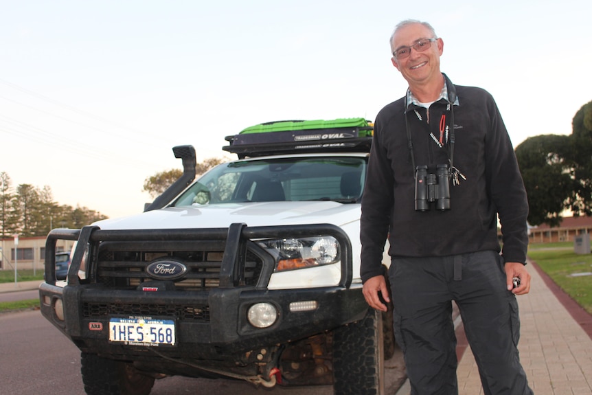 He stands by a 4WD with binoculars around his neck