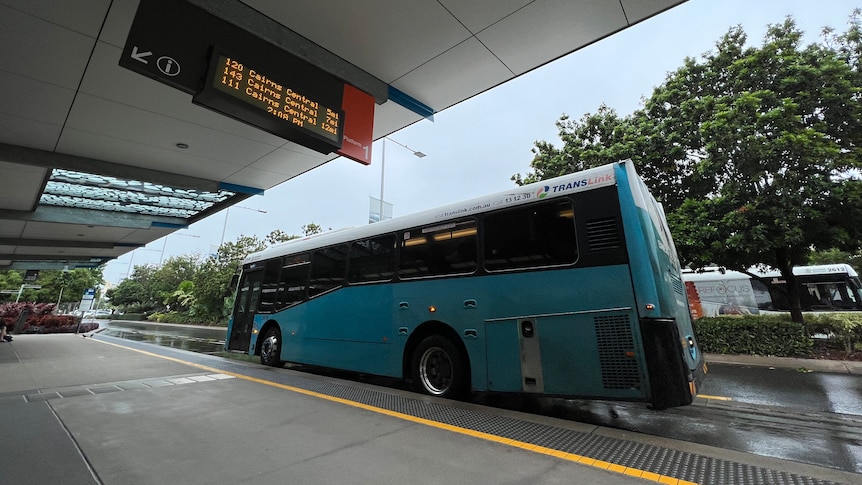 A large blue bus parked in front of a wide footpath.