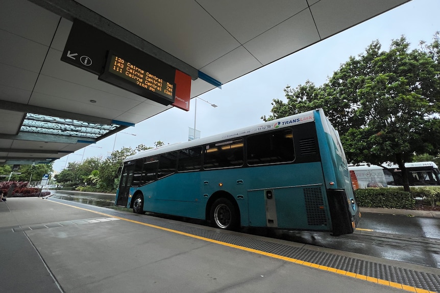 A large blue bus parked in front of a wide footpath.