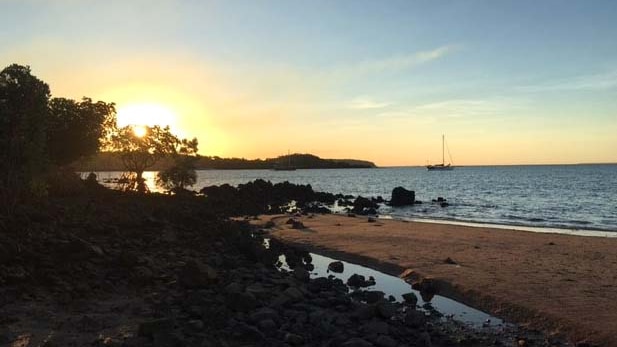 An image of the Kimberley coastline, with a yacht at anchor and the sun setting in the background.