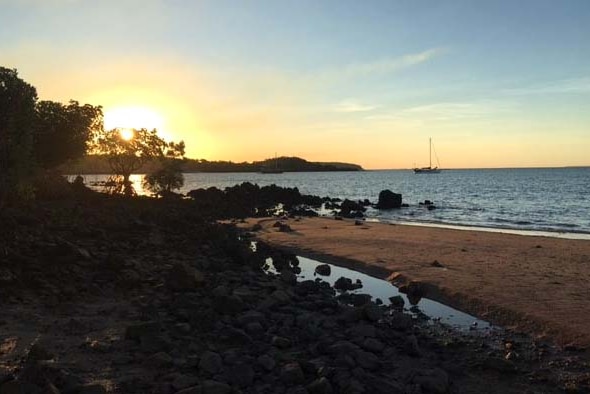 An image of the Kimberley coastline, with a yacht at anchor and the sun setting in the background.