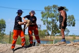 An old man in a black singlet, shorts and hat with a man and a woman wearing orange pants