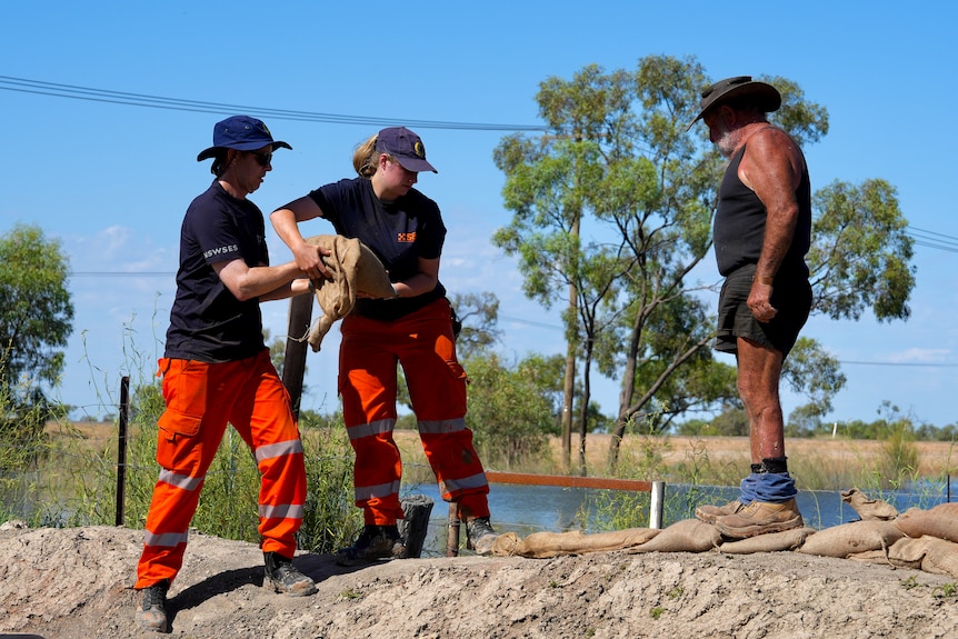 An old man in a black single, shorts and hat with a man and a woman wearing orange pants