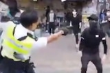 A grainy image from a social media video showing a police officer pointing a gun at a protester, who has their face covered.