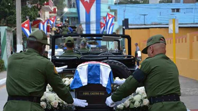 A black box with Fidel Castro Ruz's name on it sits in the back of an army car as two military men stand guard.