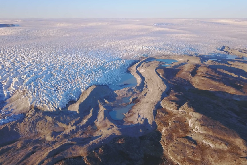 An aerial view showing the Greenland ice sheet meeting bare land.