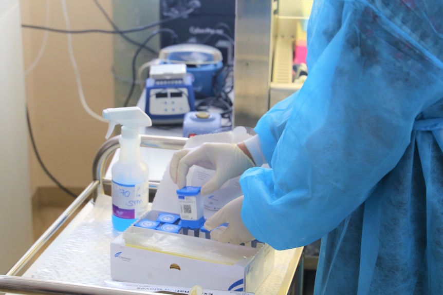 A man wearing scrubs and gloves picks up a plastic container from a tray of equipment.