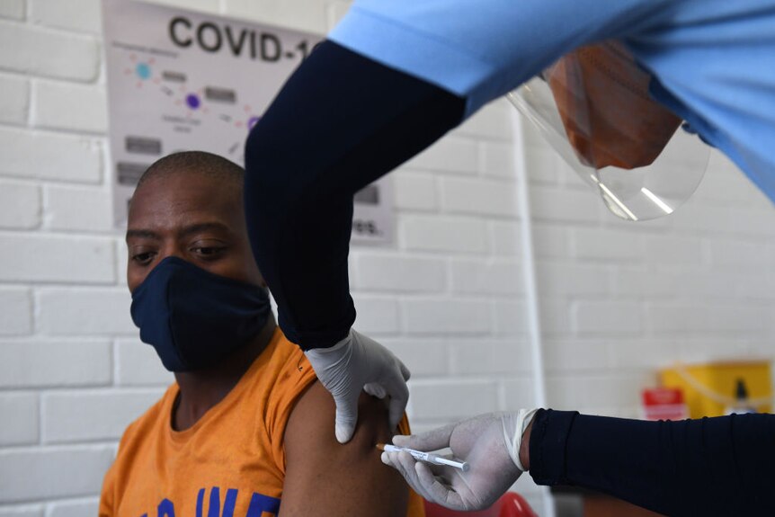 A black African man gets a needle in his arm with a COVID-19 sign in the background