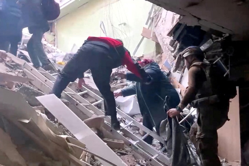 A persons is helped to climbe over rubble in Mariupol. 