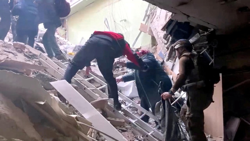 A persons is helped to climbe over rubble in Mariupol. 