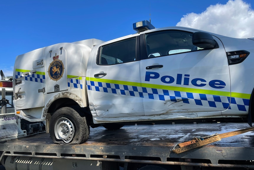 A police car with scraped side and flate tire on the back of a tow truck.