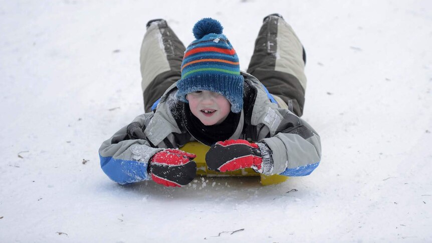 A boy toboggans down a snowy hillside