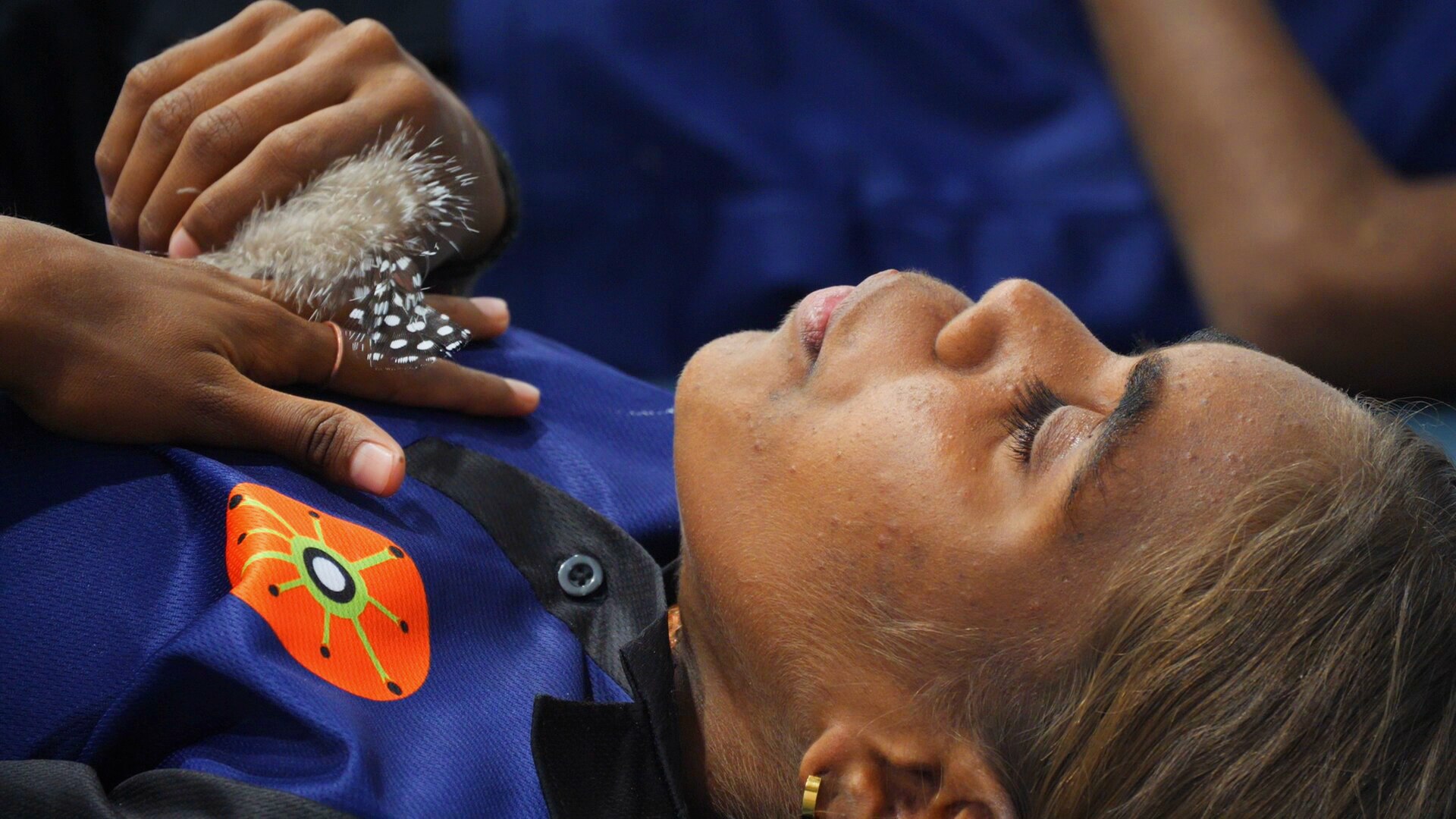 A girl lying down with her eyes closed holding a feather 