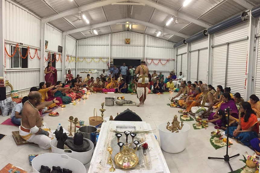 A large group of people sitting in a large rectangle shed.