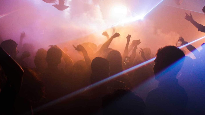A group of dancers, dancing in a club with smoke machines and pink and yellow lights.