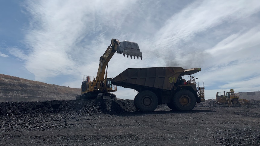 silhouetted coal mining digger next to a dump truck at a coal mine