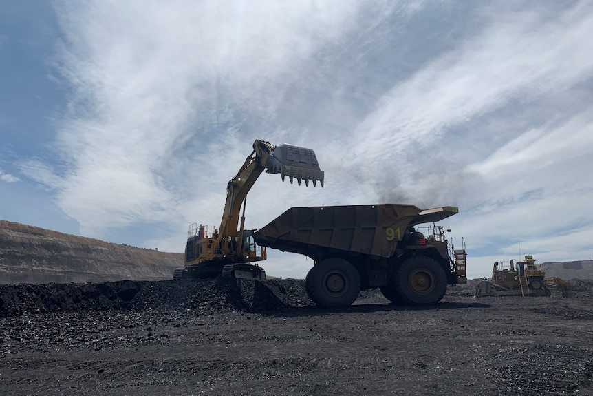 A silhouetted coal mining digger next to a dump truck at a coal mine.