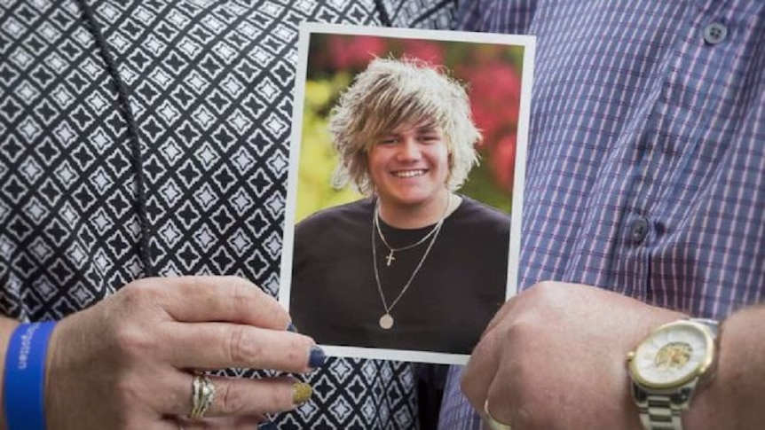 Hands holding a photo of a young man with blonde hair wearing necklaces