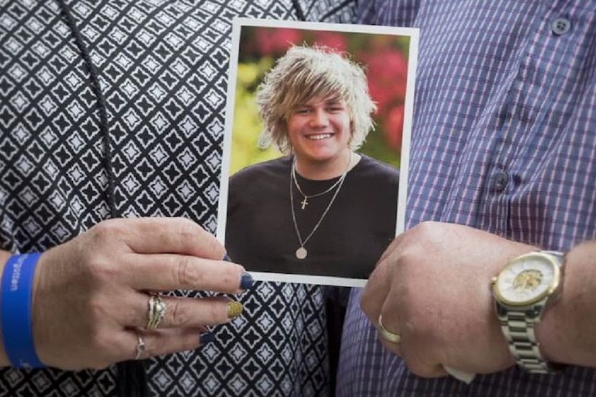 Hands holding a photo of a young man with blonde hair wearing necklaces