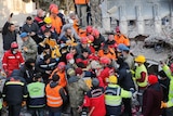 A group of rescuers crowd around as a survivor is carried from the rubble on a stretcher. 