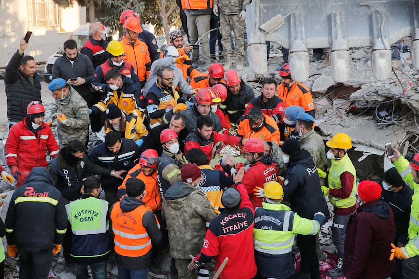 当一名幸存者被担架抬出废墟时，一群救援人员围了过来。
