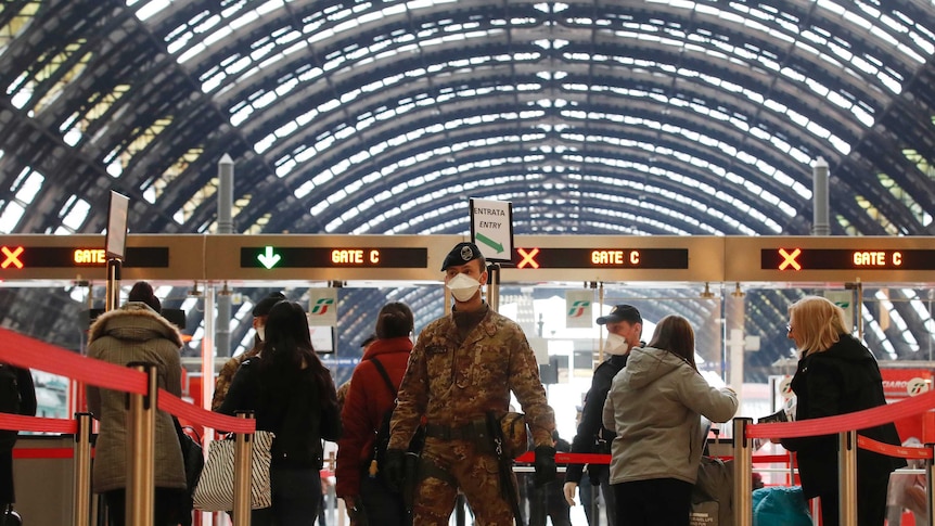 A soldier stands in front of a line of people going through a ticketing booth.