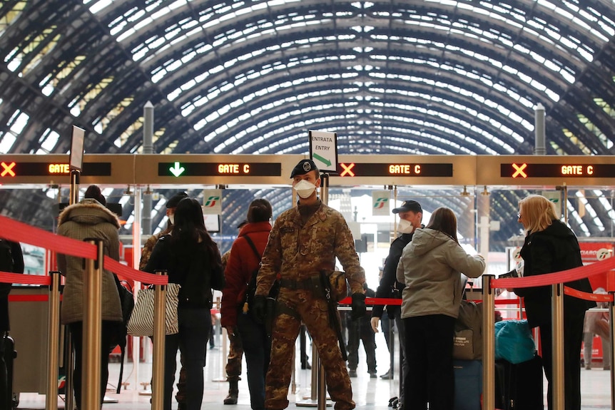 A soldier stands in front of a line of people going through a ticketing booth.