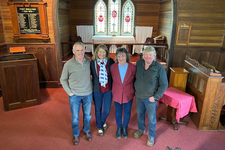 Four smiling locals stand proudly in a beautiful, wood clad church with radiant stain glass mirrors.