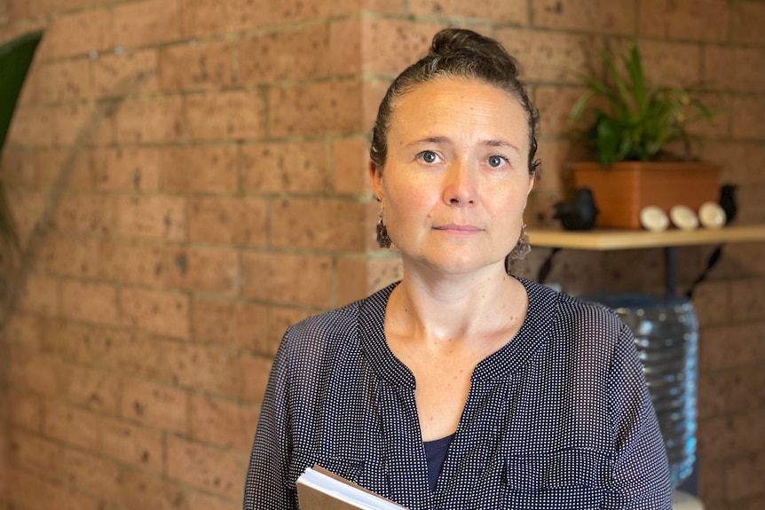 A woman with her hair tied back looking at the camera sitting in front of a brick wall