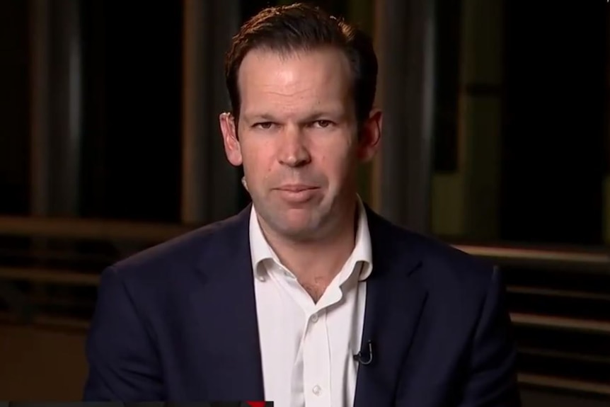 A man in a dark suit and white shirt looks forward.