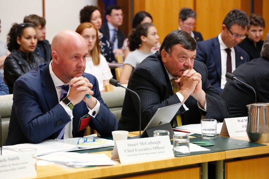 Two men at a table with a crowd of people behind them