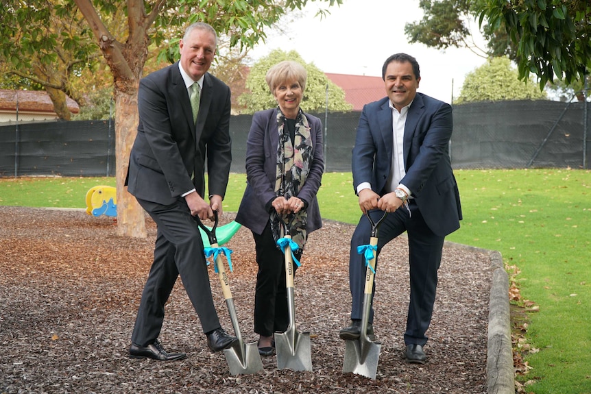Two men in suits and a woman in a jacket pose with shovels