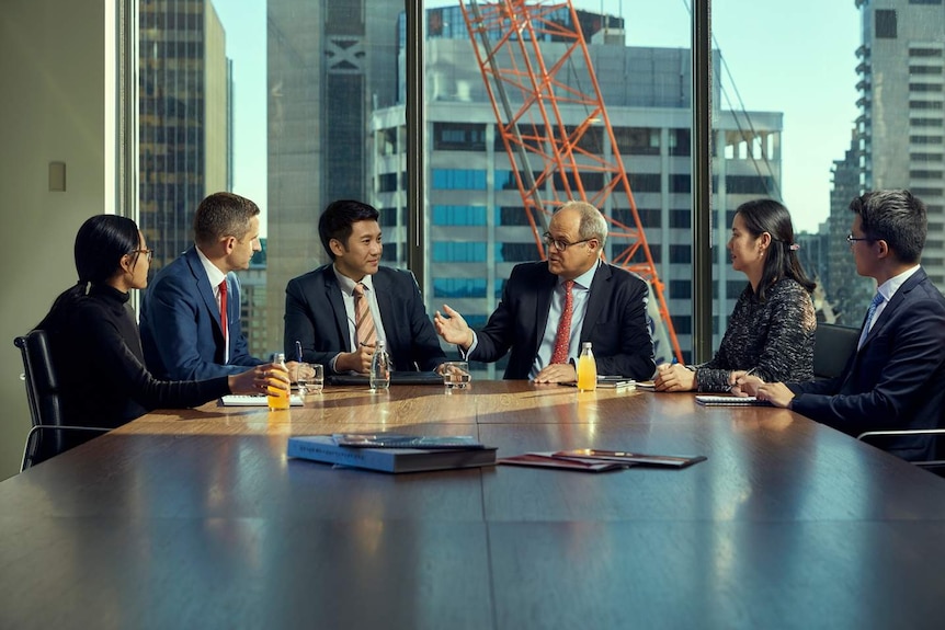 Six people sit around a CBD boardroom table