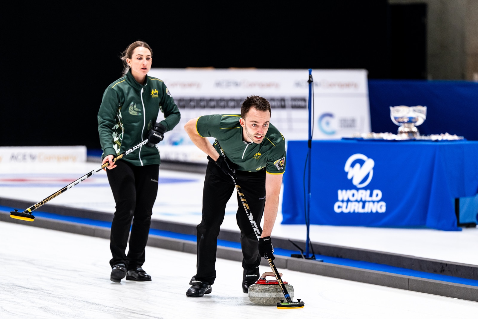 Dean Hewitt sweeps as Tahli Gill watches during curling championship.