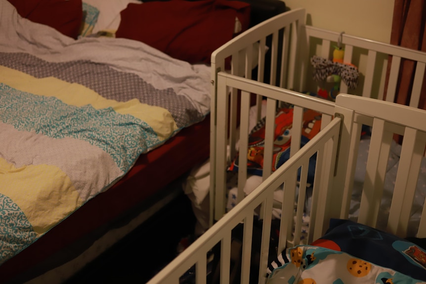 Two cots are tightly crammed into a gap between a bed and wall.